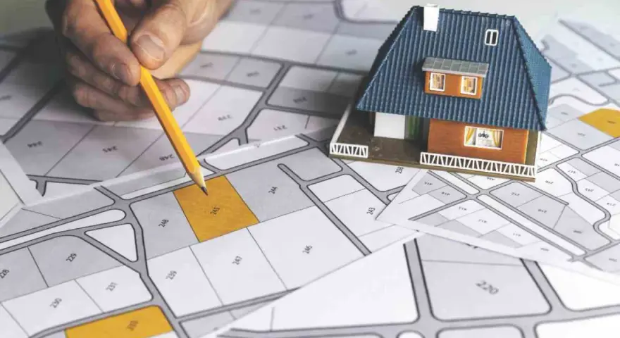 Mano con matita su mappa catastale, con modellino di casa. Pianificazione immobiliare, categoria catastale D10.
