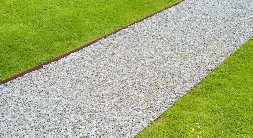 Un percorso di ghiaia bianca delimita un prato verde brillante, creando un vialetto giardino invitante.