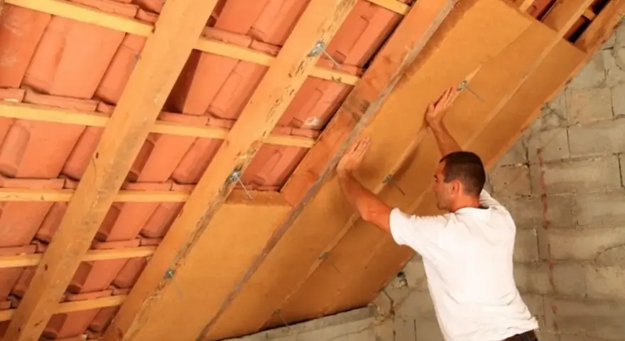 Operaio installa pannelli per la coibentazione del tetto in legno, migliorando l'isolamento termico.