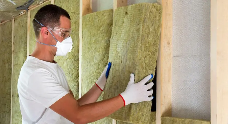 Operaio con mascherina e occhiali installa pannelli isolanti, mostrando il **coibentazione significato** per un ambiente efficiente.