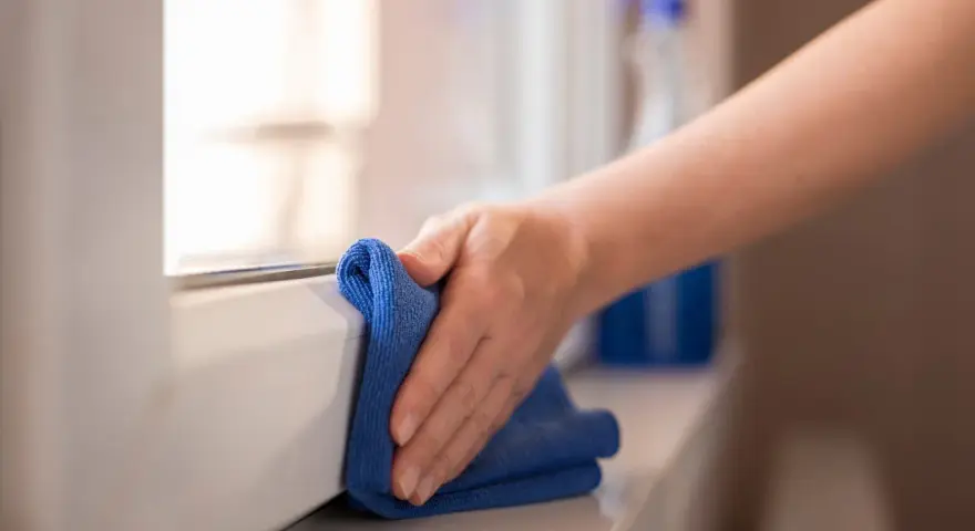 Mano pulisce davanzale in PVC effetto legno con panno blu. Scopri come pulire pvc effetto legno per mantenerlo come nuovo.