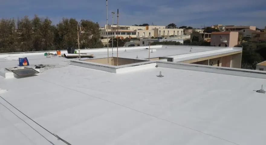 Tetto piano bianco appena impermeabilizzato senza rifarlo, con antenne e edifici sullo sfondo.
