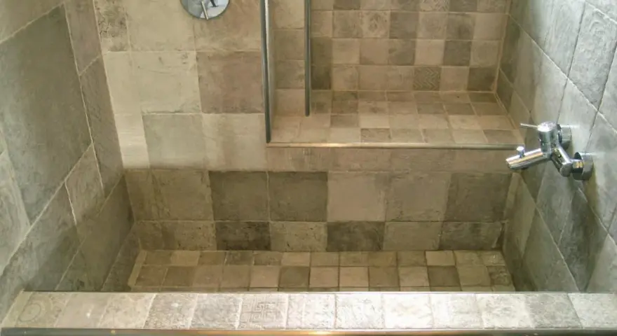 Bagno con vasca da bagno in muratura fai da te, rivestita con piastrelle grigie di varie tonalità e fantasie.