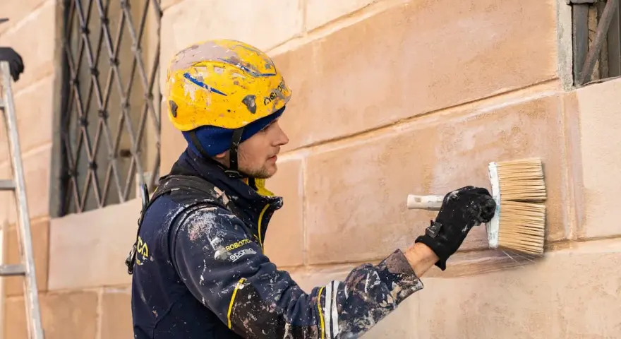 Operaio con casco giallo applica soluzione per pulire muro esterno con candeggina.
