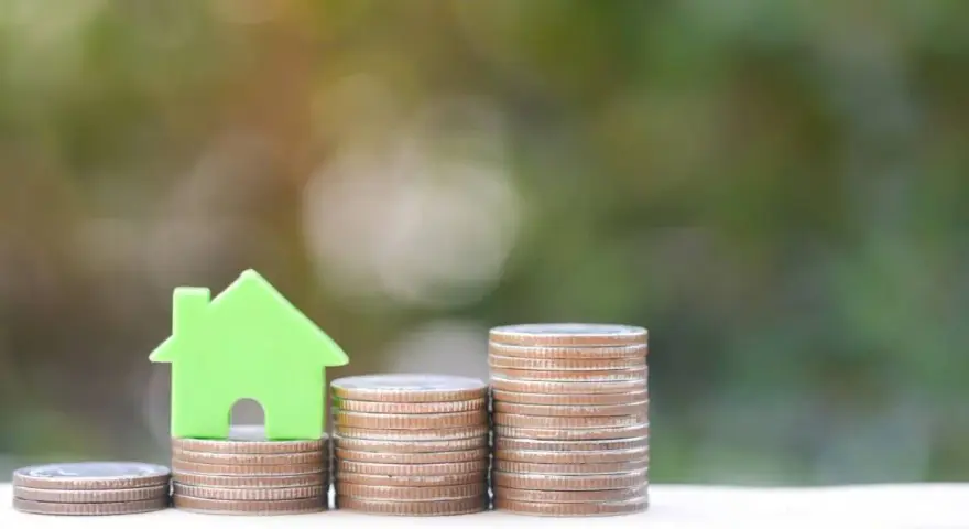 Una casa verde su pile di monete, un'immagine che simboleggia come funziona il Superbonus 110 per l'edilizia.