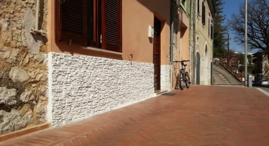 Una parete umida è stata rivestita con pietre bianche, migliorando l'estetica e la protezione dell'edificio.