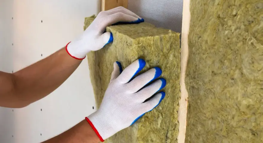 Mani guantate posizionano un pannello di lana di roccia, un materiale da **cemento isolante termico**, all'interno di una struttura in legno.