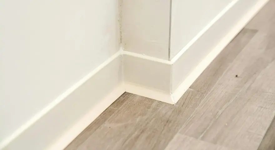 Angolo di una stanza con pavimento in laminato grigio e battiscopa bianco appena posato.