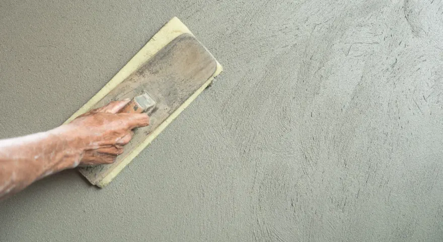 Mano che stende l'intonaco con una spatola. Dopo l'intonaco posso pitturare la parete.
