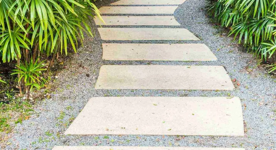 Un sentiero sinuoso con lastre di pietra e ghiaia, circondato da vegetazione lussureggiante. Idee marciapiede casa per un ingresso accogliente.