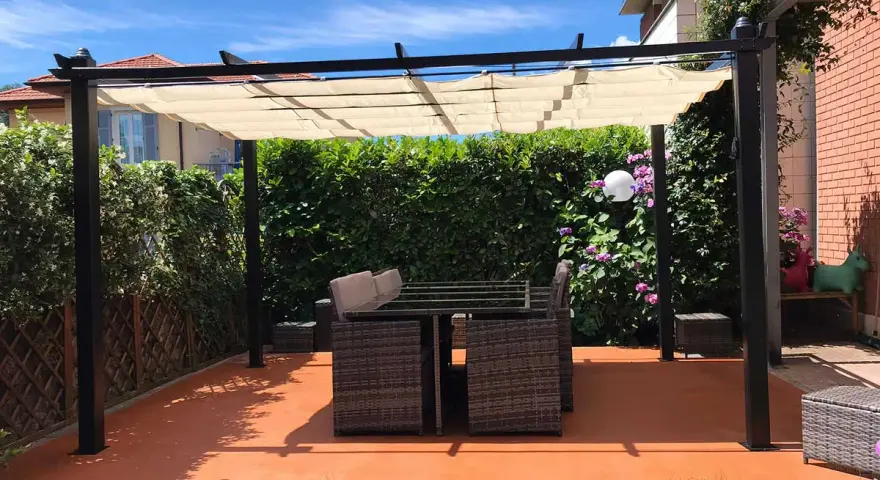 Un patio con tavolo e sedie sotto una pergola, con un **pavimento esterno economico fai da te** color terracotta.