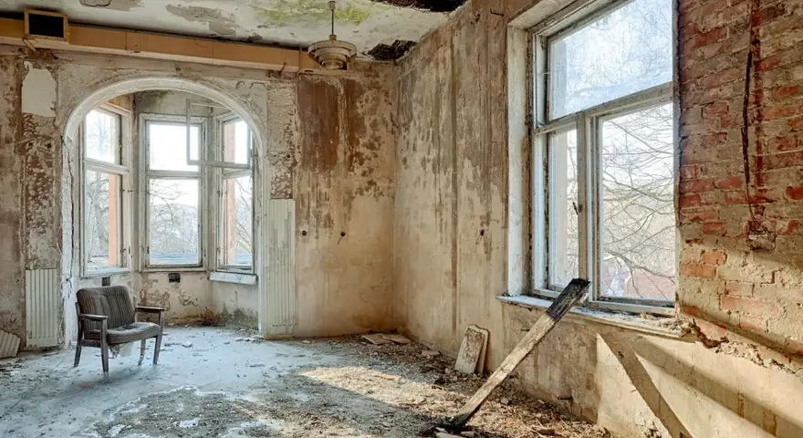 Interno di una casa a botte in rovina, con pareti scrostate, soffitto sfondato e un vecchio mobile.