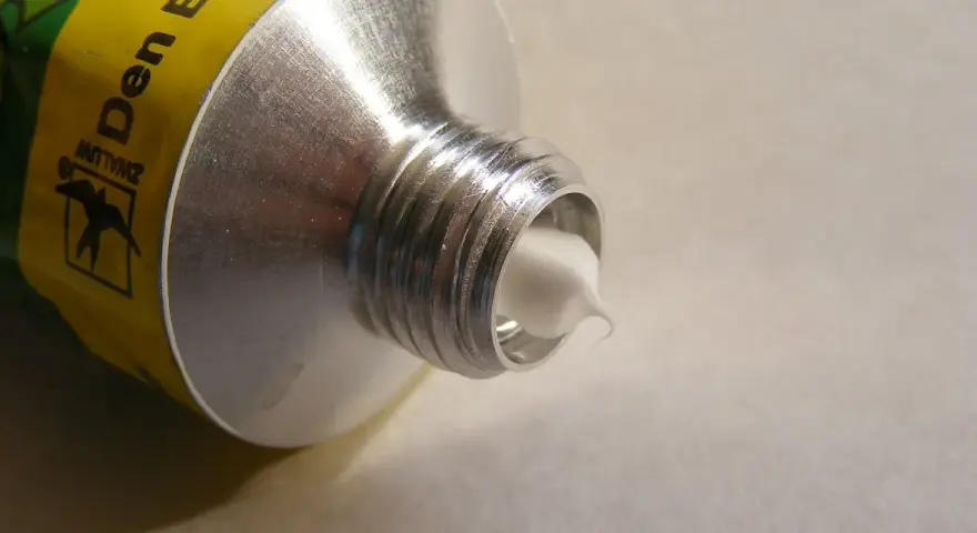 Tubo di alluminio con crema bianca che fuoriesce, mostrando diversi tipi di silicone.
