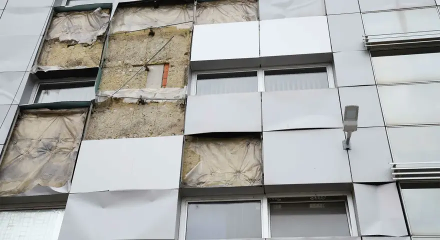 Facciata di un edificio con pannelli rimossi, mostrando l'isolamento. Si valuta la conducibilità termica dei materiali per l'efficienza energetica.