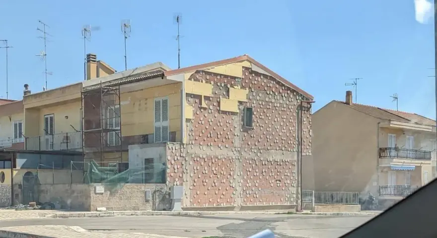 Edificio in fase di ristrutturazione, con facciata parzialmente scoperta che rivela la muratura. Sembra un condominio in attesa del suo nuovo cappotto.