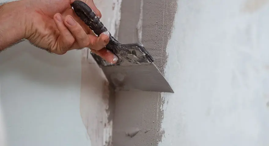 Mano che usa una spatola per stuccare un muro, creando una superficie liscia e uniforme per la pittura.