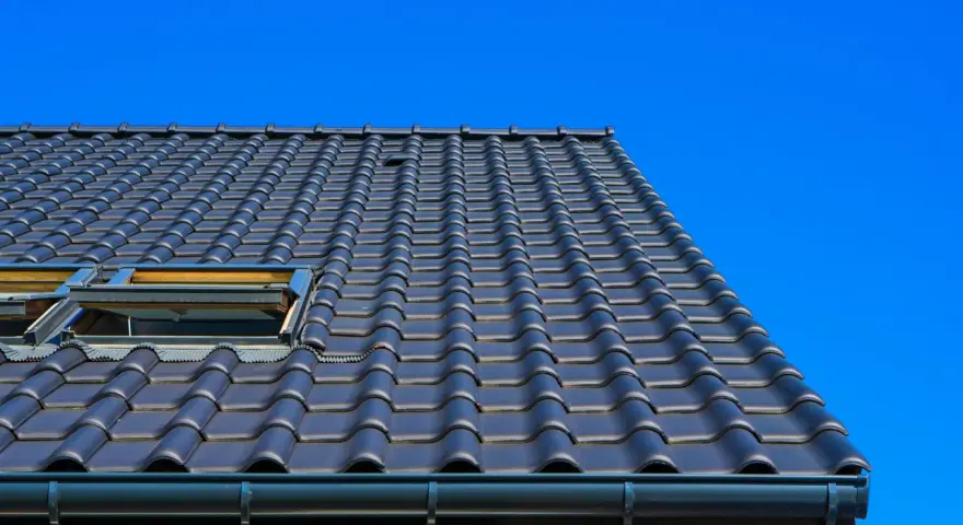 Coperture tetti moderni in tegole scure, con lucernari a vista sotto un cielo azzurro intenso.