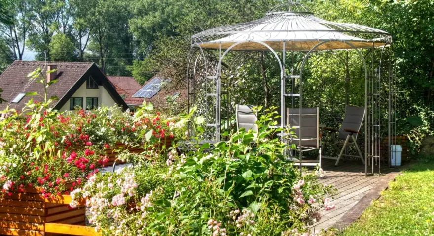 Un gazebo con un pavimento in legno fai da te, circondato da fiori colorati e vegetazione lussureggiante.