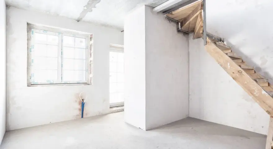 Interno grezzo con finestra, porta finestra e scala in legno grezzo. Ambiente in fase di ristrutturazione, un futuro piano seminterrato.