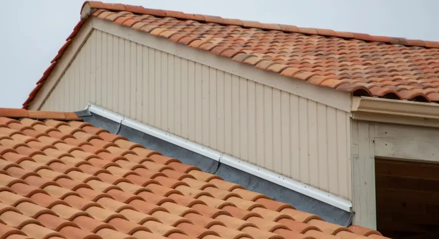 Tegole rosse su un tetto, con pannelli verticali beige e una grondaia. Le scossaline proteggono il bordo del tetto.