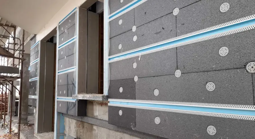 Pannelli grigi per cappotto termico ignifugo, fissati con tasselli bianchi e profili azzurri, in fase di installazione su un edificio.