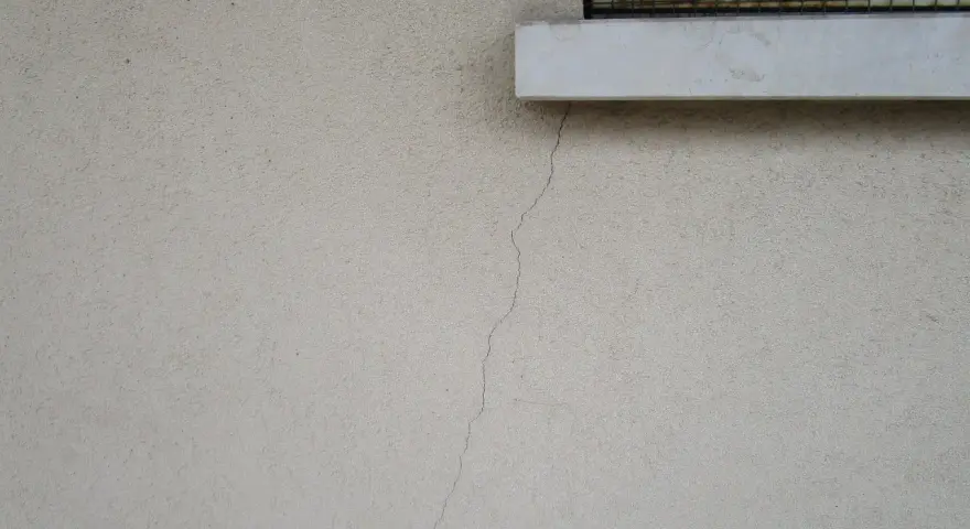 Crepa sottile su muro esterno, vicino a davanzale e inferriata. Necessaria riparazione crepe strutturali.
