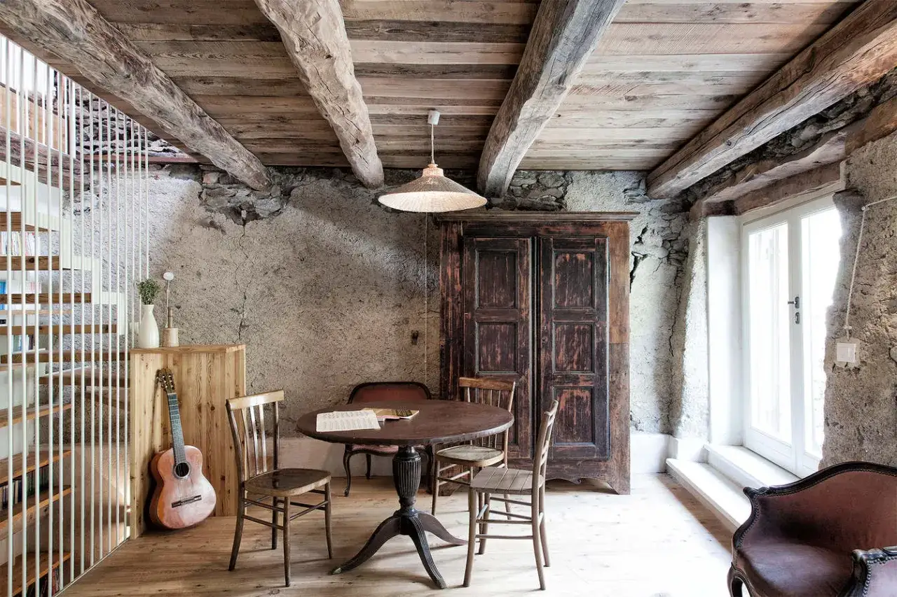 Idee per ristrutturare casa di montagna: un salotto rustico con travi a vista, mobili antichi e una chitarra.