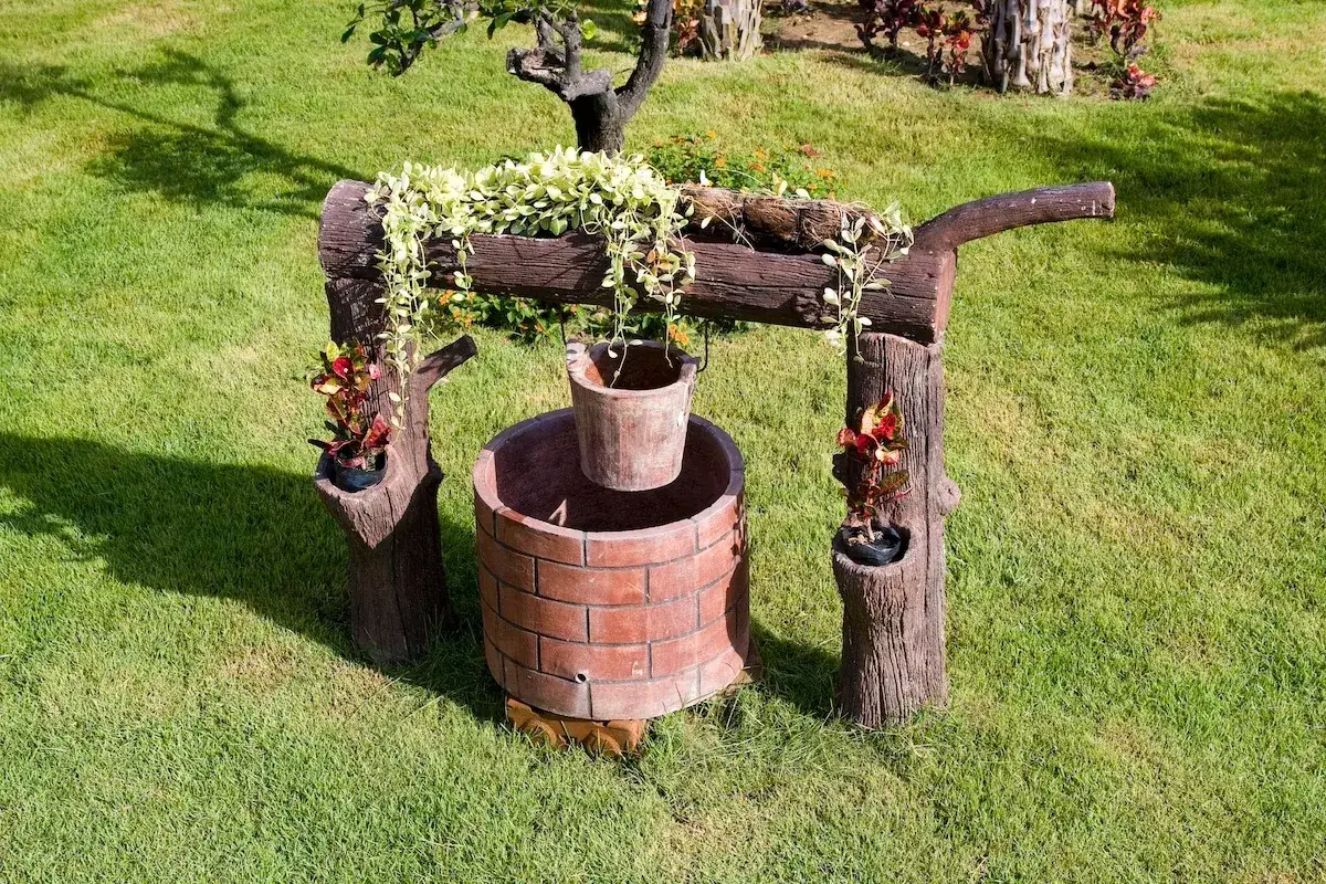 Pozzo decorativo in mattoni con secchio appeso, circondato da erba verde. Chiss&agrave; quanto costa fare un pozzo cos&igrave;!