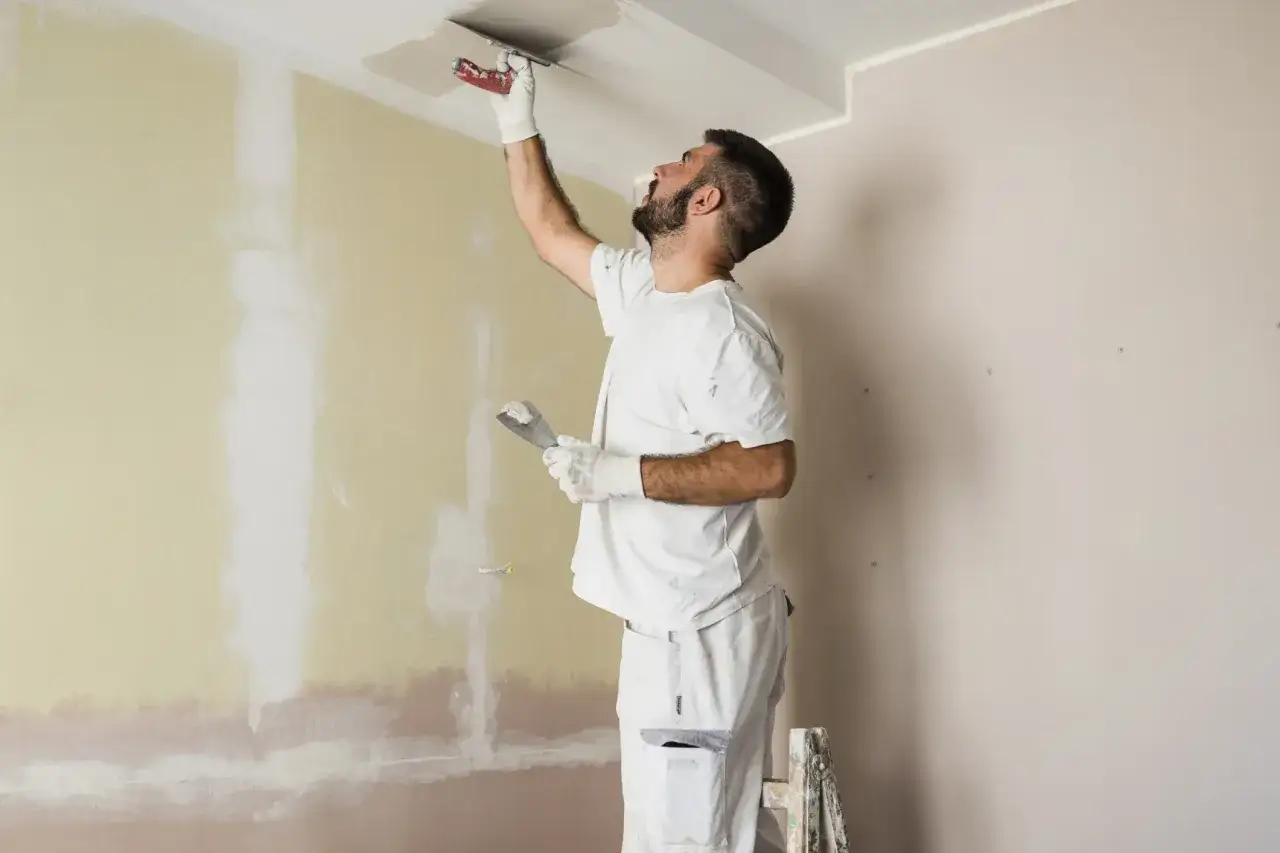Un imbianchino sta stendendo lo stucco sul soffitto. Dopo l'intonaco posso pitturare, il lavoro procede bene.