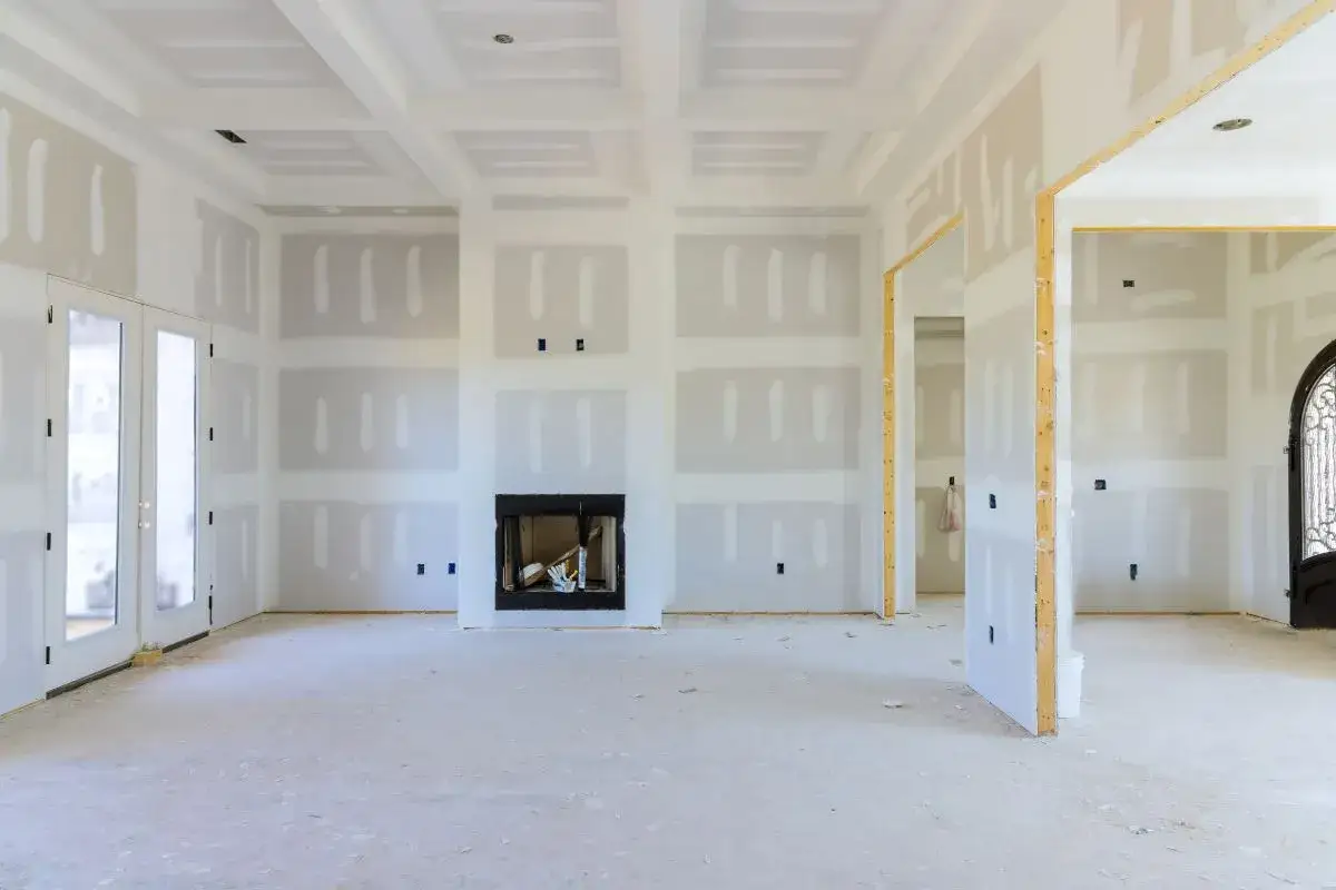 Interni in fase di finitura, con pareti rivestite con cartongesso senza telaio, camino centrale e porte in vetro.