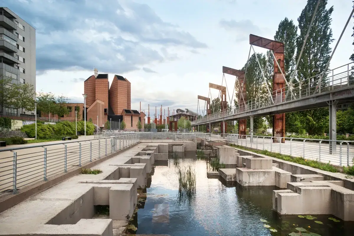 Un'area urbana rigenerata con un canale, un ponte metallico arrugginito e edifici moderni in mattoni rossi. Un esempio di legge sulla rigenerazione urbana.