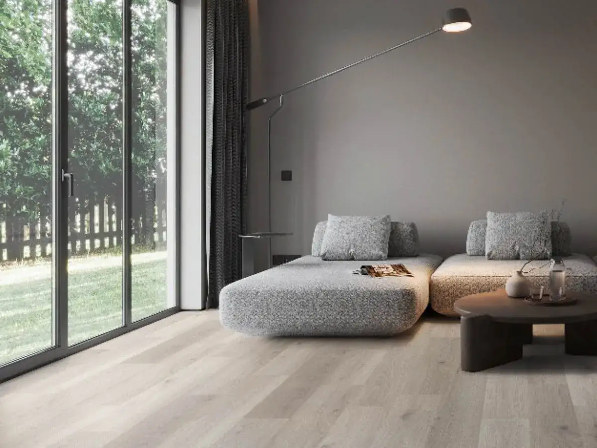 Soggiorno moderno con divani grigi e un tavolino, illuminato da una grande finestra che si affaccia sul verde. I migliori pavimenti per interni in legno chiaro completano l'ambiente.