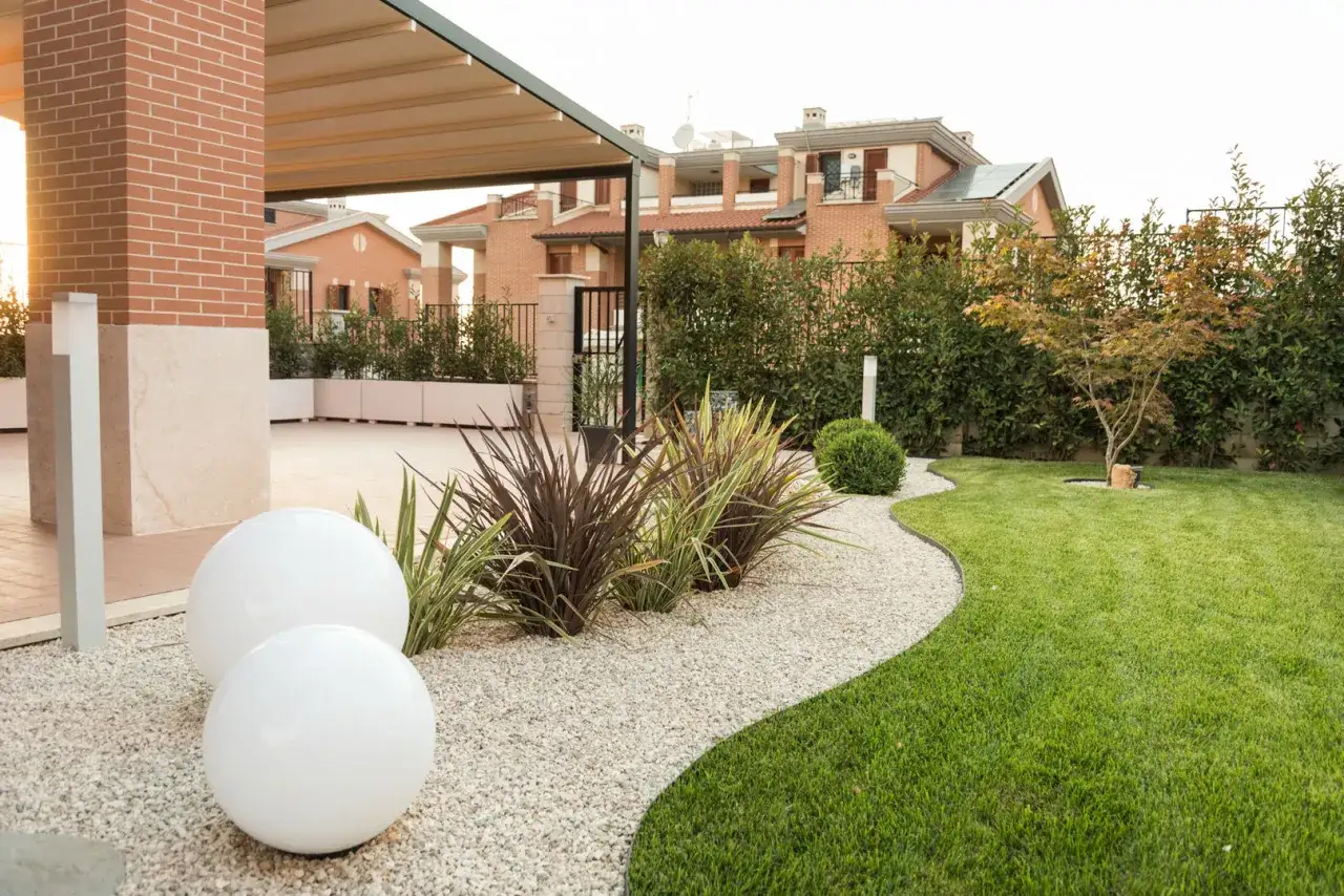 Giardino moderno con ghiaia bianca, sfere luminose e piante ornamentali. Un'idea per creare un'oasi di pace con sassi bianchi.