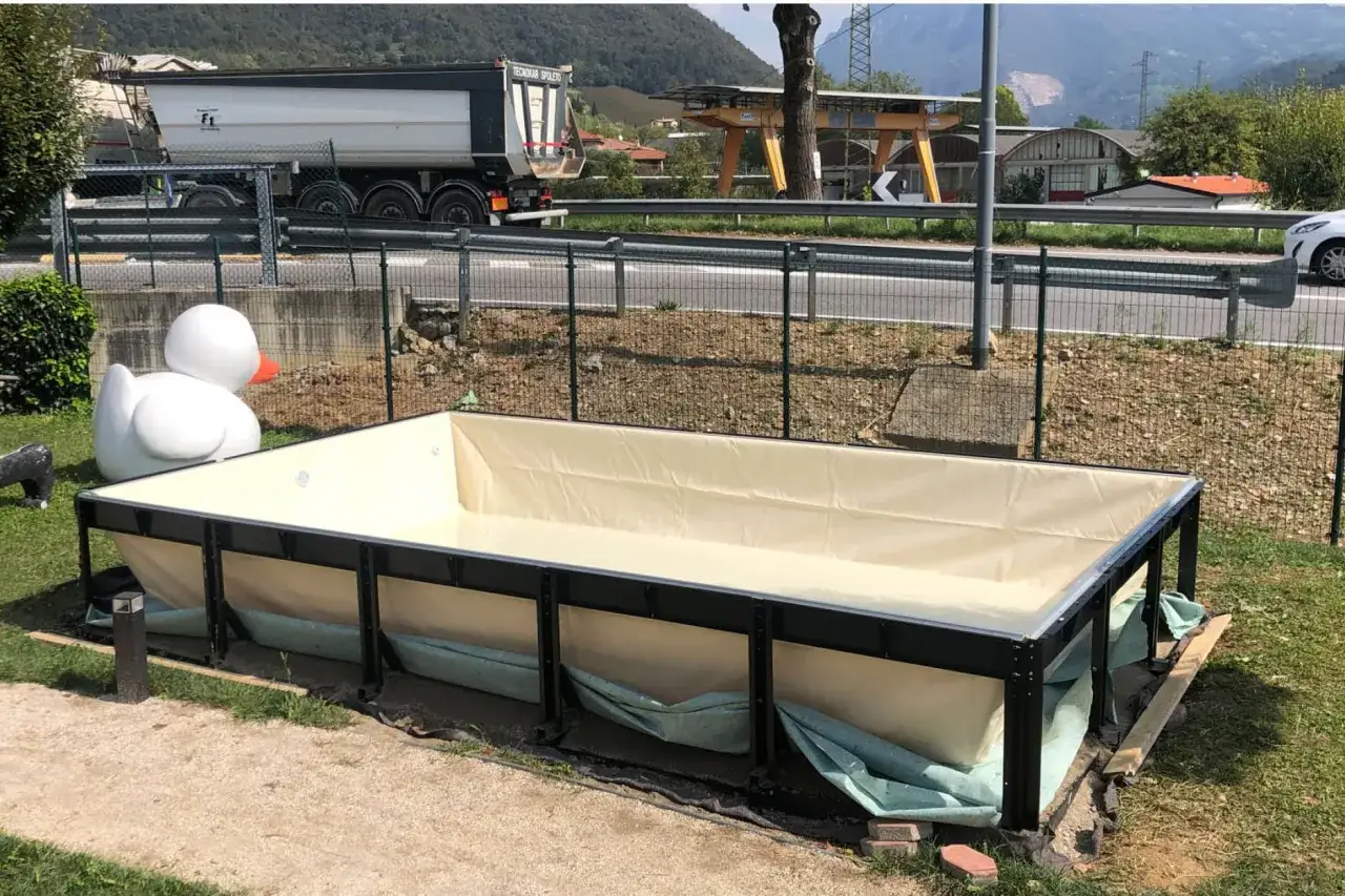 Una grande piscina fuori terra, forse una piscina senza permessi, &egrave; in fase di installazione in un giardino. Accanto, un'enorme papera gonfiabile bianca.