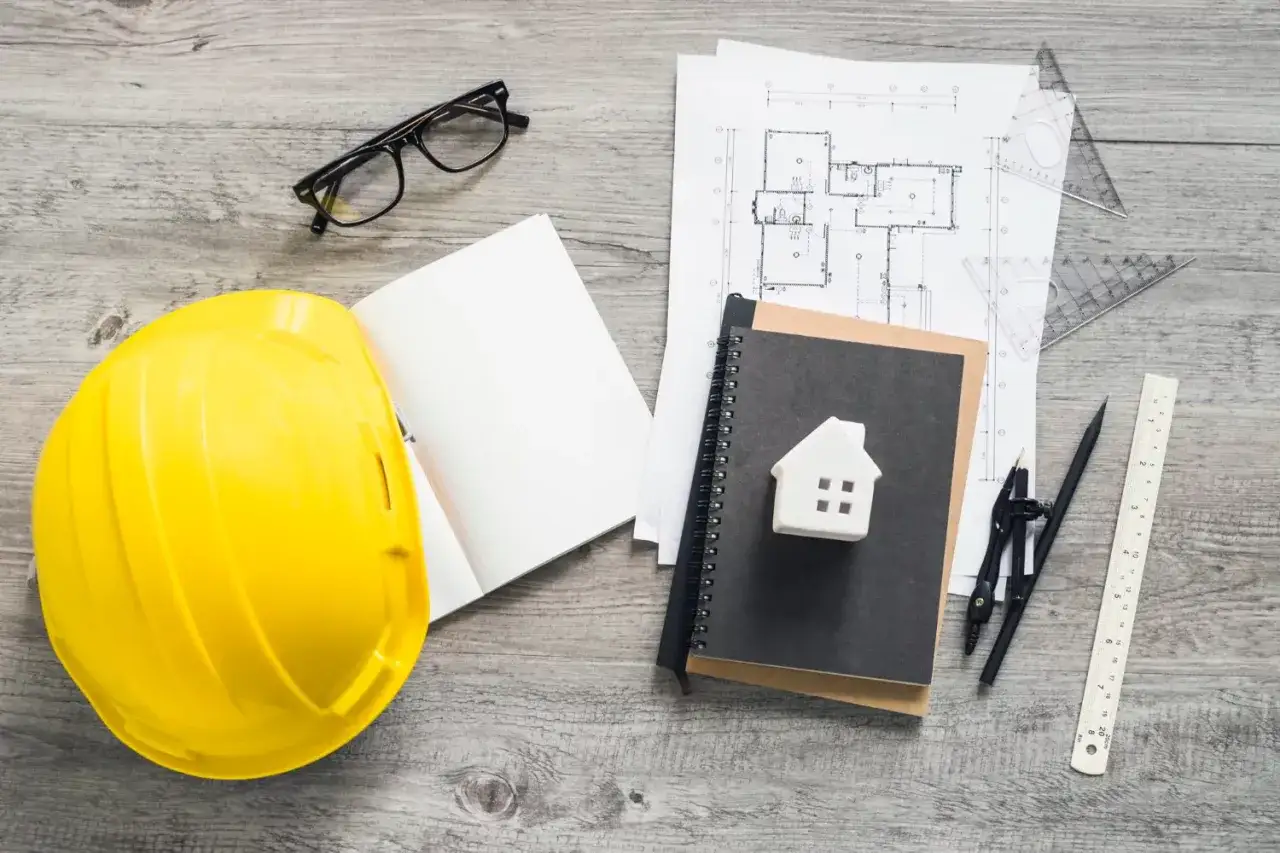 Casco giallo, occhiali, disegni tecnici e un modellino di casa: tutto pronto per definire l'esempio capitolato casa nuova costruzione.