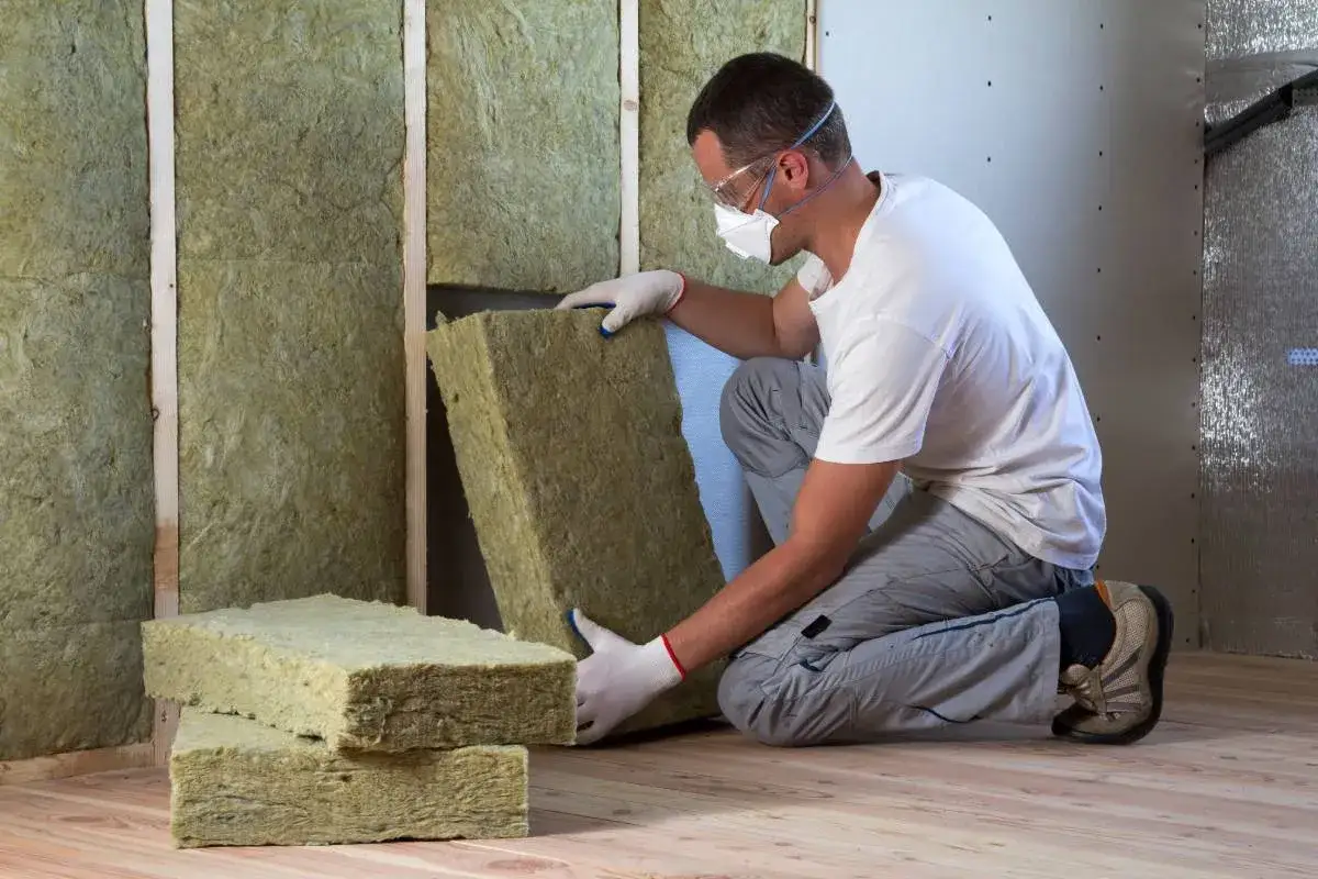 Operaio installa pannelli di lana di roccia per isolamento termico e acustico. La lana di roccia a cosa serve? A creare ambienti confortevoli e sicuri.