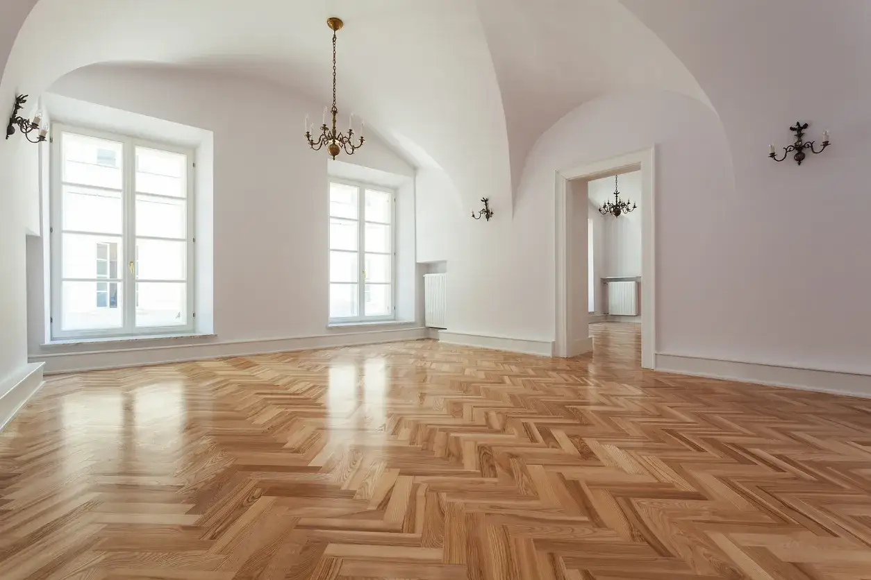 Un parquet a spina di pesce lucido, pronto per il levigare parquet fai da te. L'ambiente &egrave; luminoso, con grandi finestre e lampadari d'epoca.
