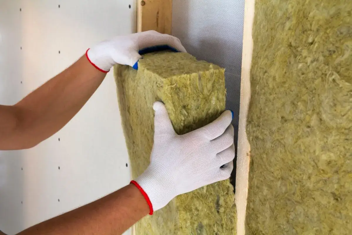 Mani guantate posizionano un pannello isolante in lana di roccia, creando un cappotto interno o esterno per un'efficace coibentazione.