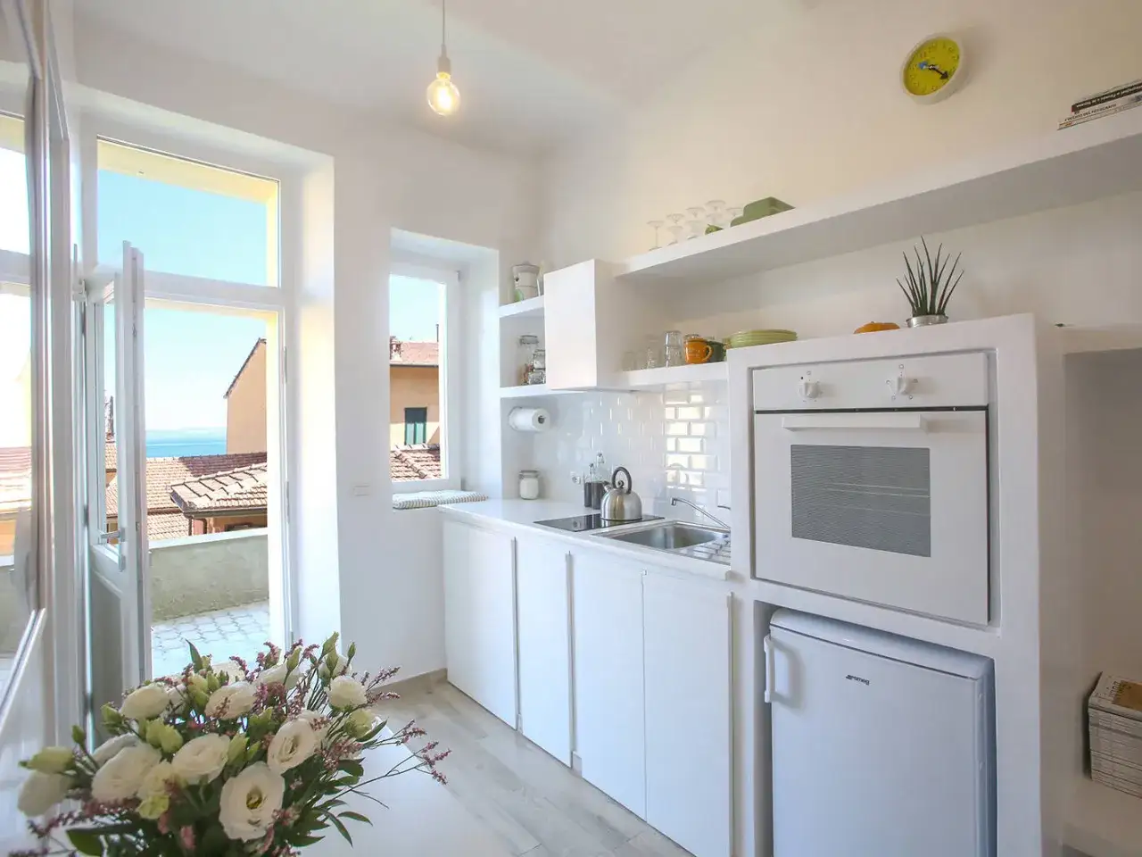 Cucina luminosa con vista mare, perfetta per idee ristrutturazione casa al mare. Bianco, minimalista, con forno e frigo Smeg.