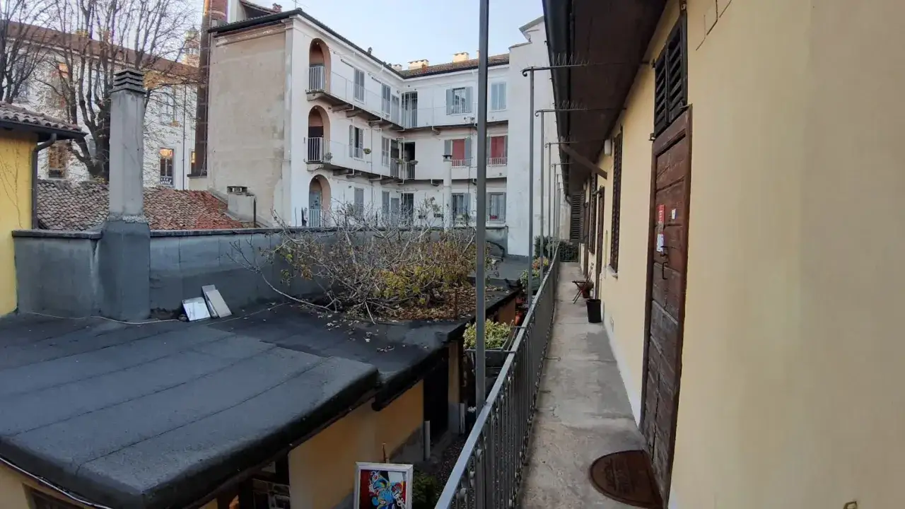Cortile interno con case di ringhiera, balconi, camini e un albero spoglio.