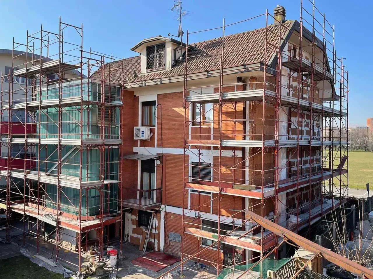 Edificio in ristrutturazione con ponteggi rossi. Si vedono mattoni a vista e finestre verdi. Case green cosa sono? Un futuro sostenibile in costruzione.