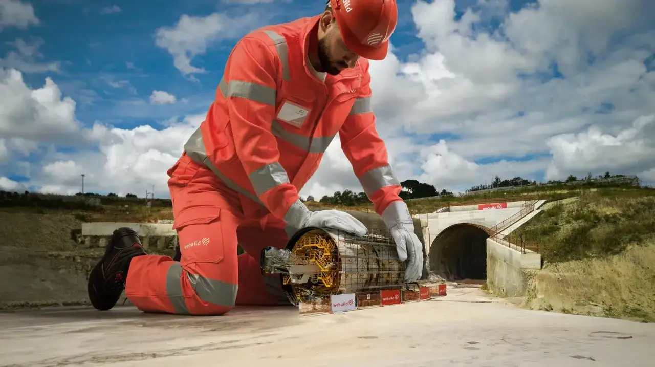 Operaio in tuta arancione esamina una fresa meccanica, simbolo de i migliori general contractor che costruiscono infrastrutture.
