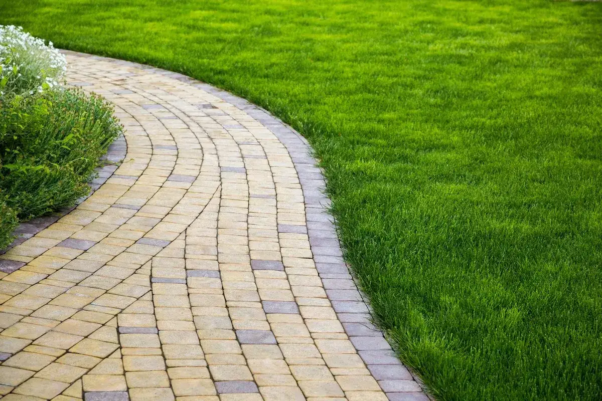 Un curvo vialetto giardino in pietra conduce attraverso un prato verde brillante, fiancheggiato da cespugli rigogliosi.