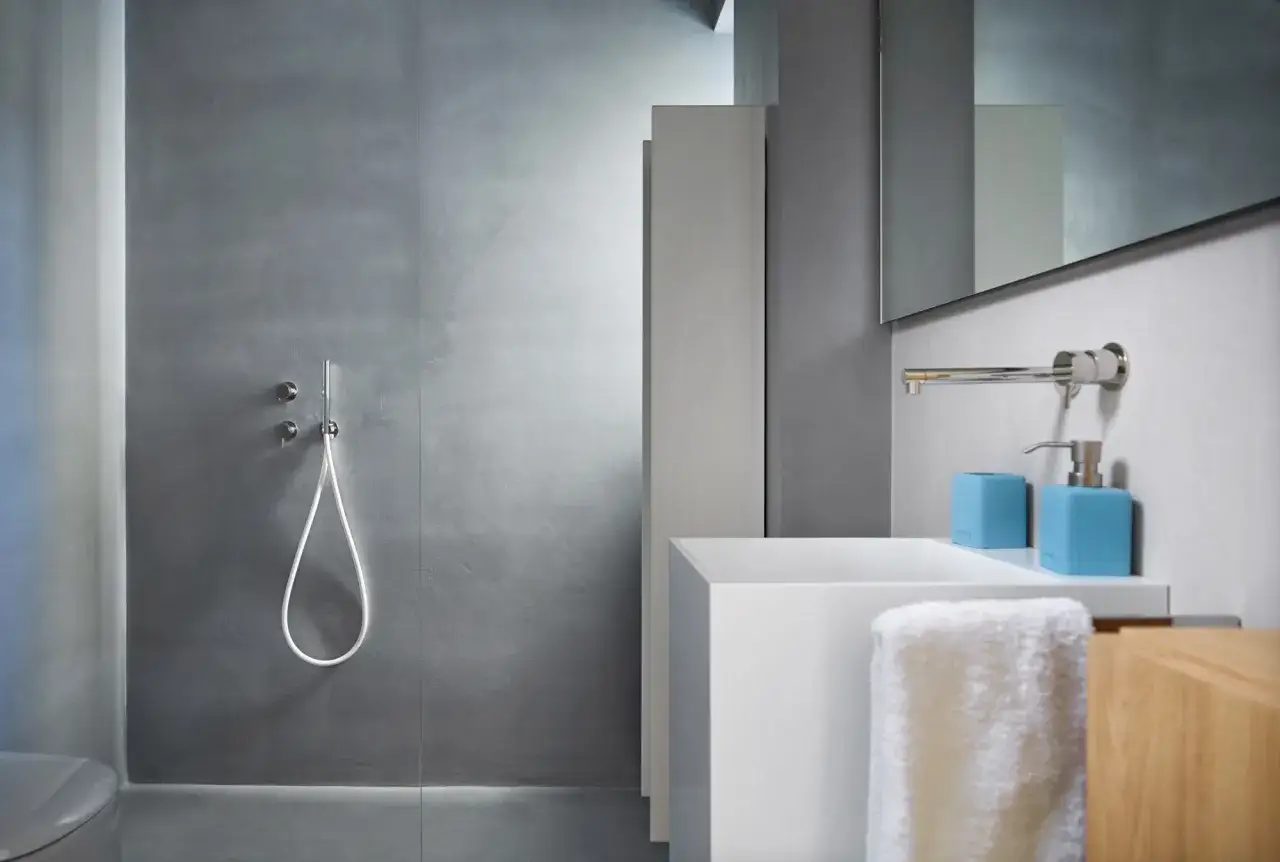 Bagno moderno con doccia con rivestimento senza piastrelle effetto resina, lavabo bianco e accessori azzurri.
