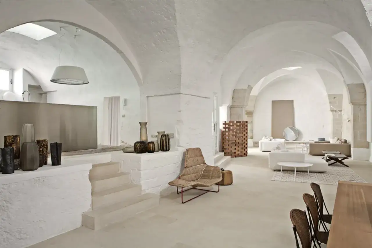 Interno moderno con soffitti a botte, divani bianchi, sedie in vimini e vasi decorativi.