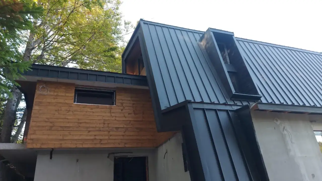 Tetto in metallo scuro con scossaline che proteggono le pareti in legno e cemento.