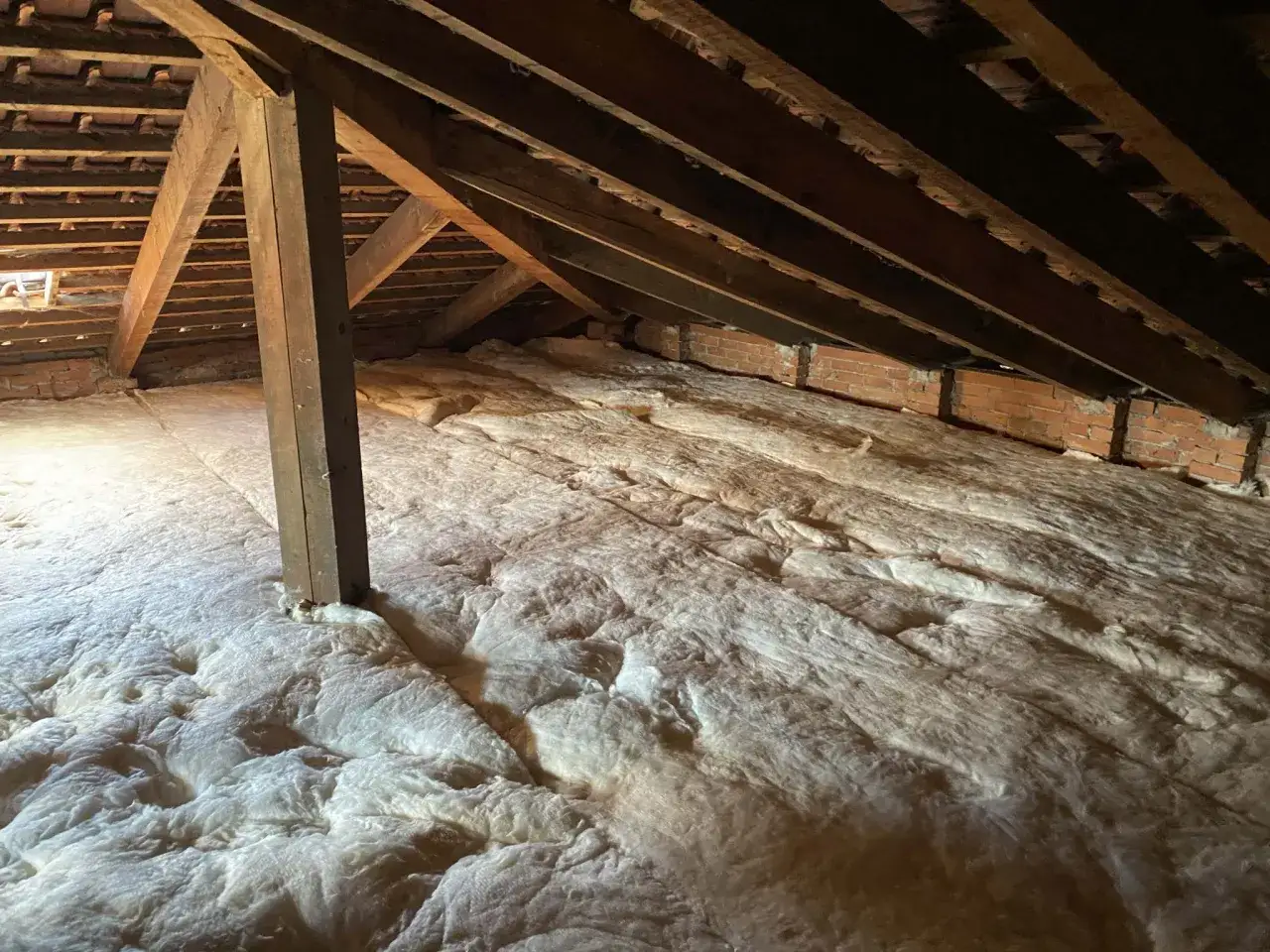Sottotetto in fase di isolamento con spessa lana di roccia per sottotetto, tra travi in legno e mattoni a vista.