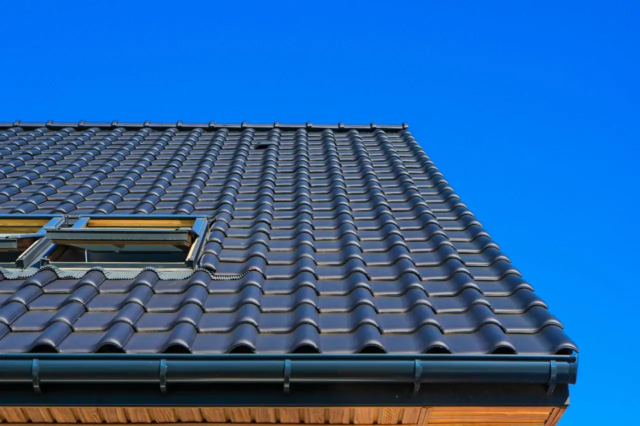 Coperture tetti moderni in tegole scure, con lucernari integrati, sotto un cielo azzurro brillante.